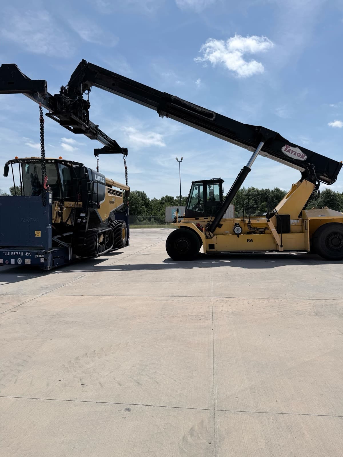 Reach stacker parked alongside the harvester, boom raised before the lift