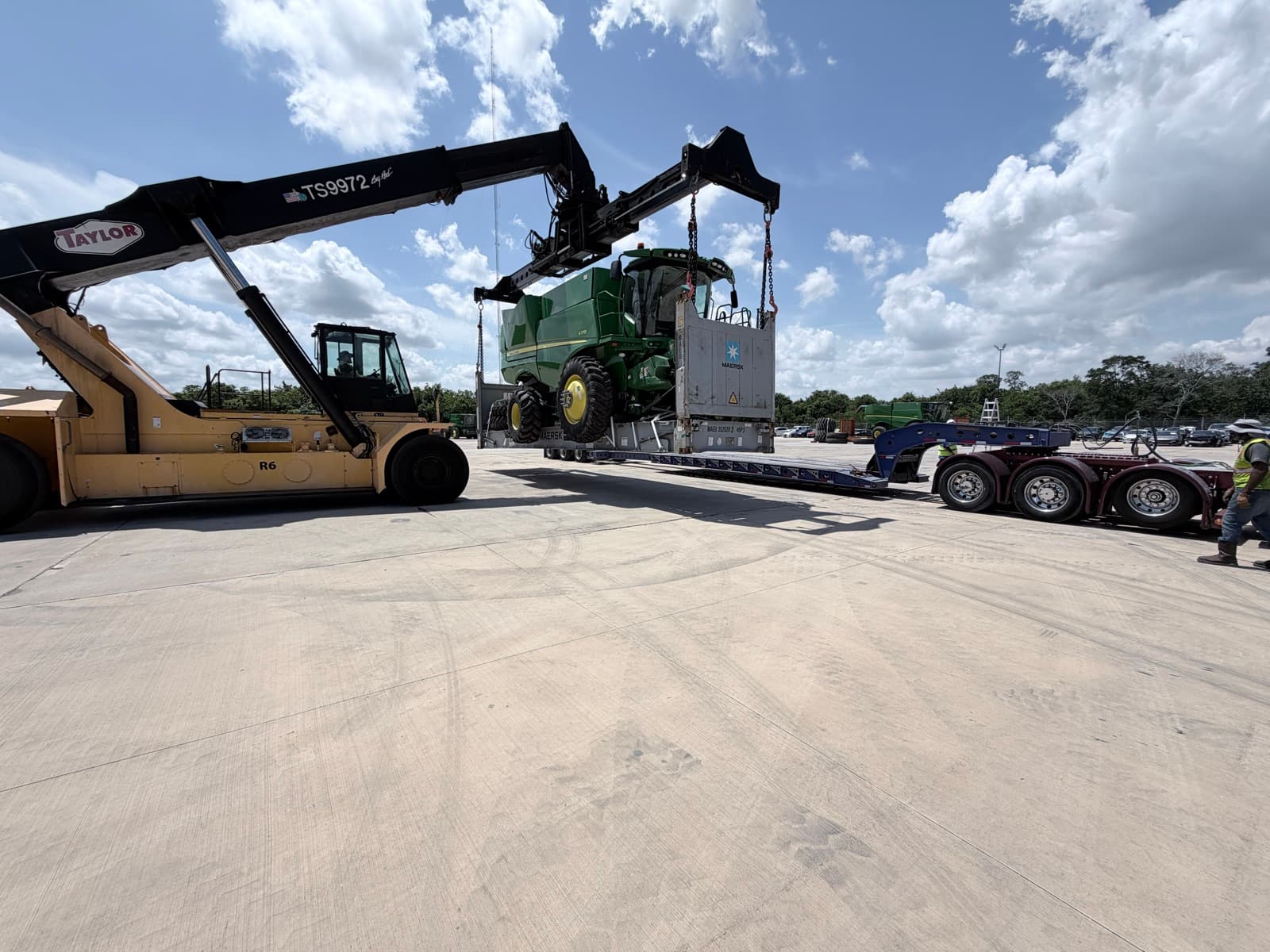 Wide view of the reach stacker, flat rack, and lowboy staged across the yard