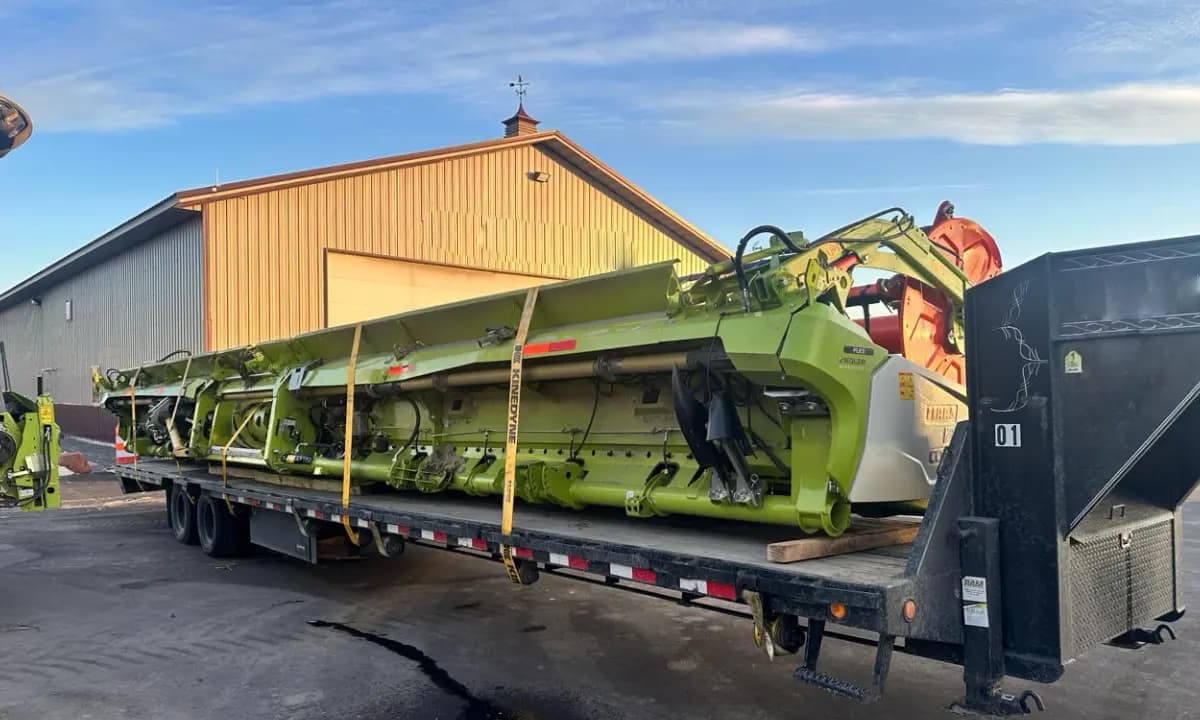 A harvester header strapped to a trailer beside the warehouse as the crew works.