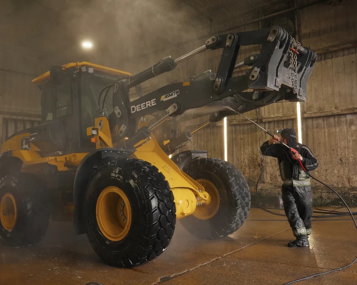 A crew member pressure-washing a wheel loader in the wash bay.