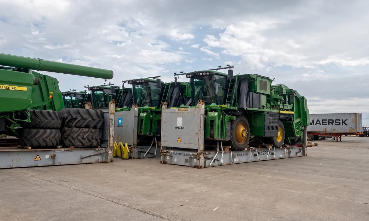 A row of combines staged on the tarmac beside a container.