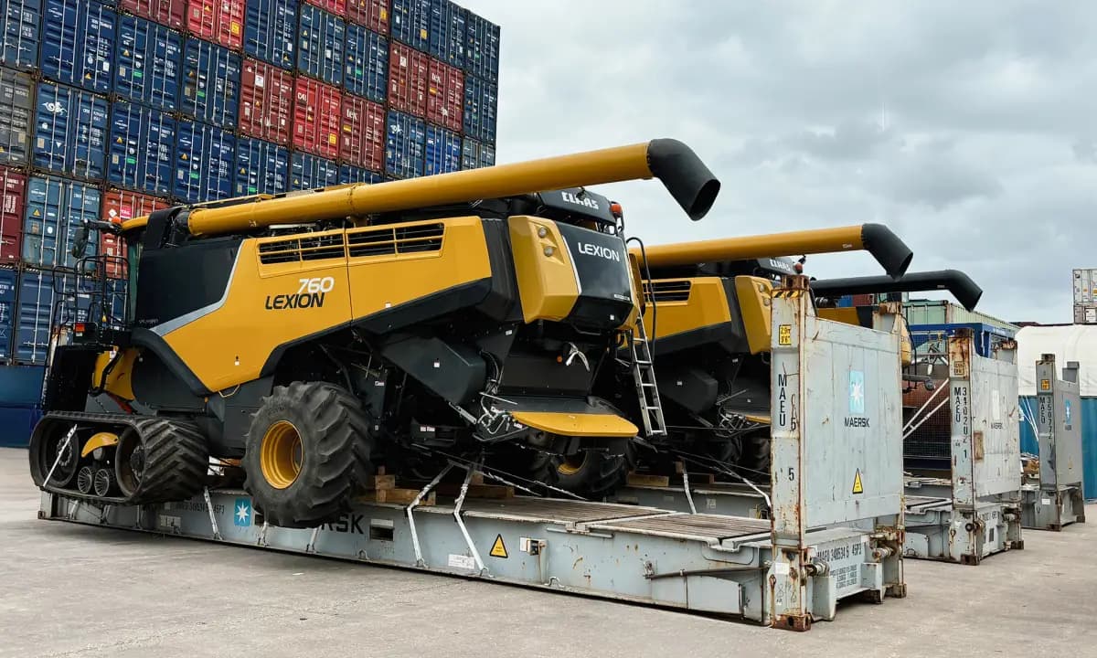 A harvester on a flat rack in front of stacked containers at the terminal.