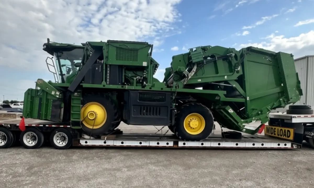A cotton harvester on a flatbed trailer under an oversize load banner.