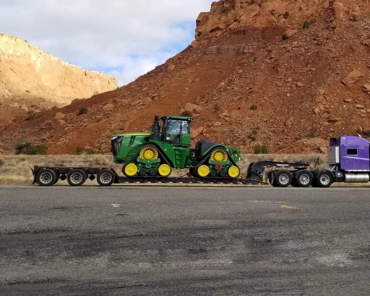 A tracked tractor on a lowboy trailer on the road through red rock country.