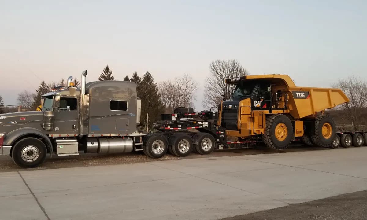 An articulated dump truck riding a lowboy trailer behind a heavy-haul tractor.